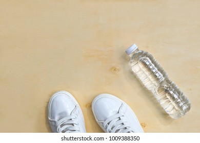 1 Pair Of White Sneakers And 1 Bottle Of Water. Placed On A Light Brown Wood Floor. Concept: Sports ,Fitness , Running ,Health  And Exercise. Zumba Dance Workout For Weight Loss.