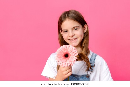 1 white girl 10 years old in a white jacket with a pink gerbera flower in her hands on a pink background smiling