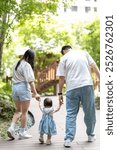 A 1 year old Taiwanese girl walking hand in hand with her parents, a man and woman in their 20s, on a hot sunny day in the streets of Taichung City, Taiwan, in September.