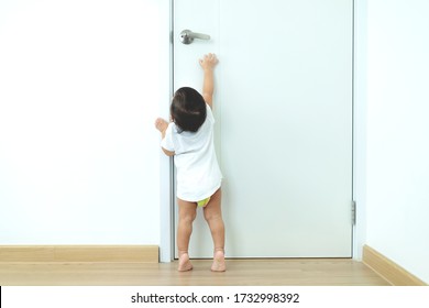 1 Year Old Toddler Asian Baby Boy Standing On Tiptoes Reaching Up Try To Open Door Knob,Security And Safety Child Concept.