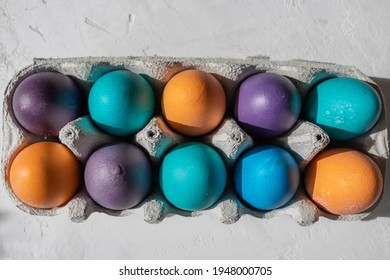 10 Colorful Easter Eggs In Blue, Turquoise, Purple, And Orange In An Egg Carton.