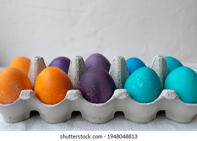 10 Colorful Easter Eggs In Blue, Turquoise, Purple, And Orange In An Egg Carton.