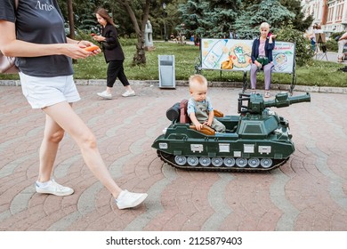 10 July 2021, Novosibirsk, Russia: Kid rides in a radio-controlled toy children military tank. The concept of militarization and parenting