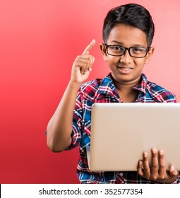 10 year old indian kid with spectacles holding  laptop in hand, posing over red background