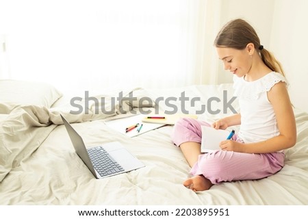 10 years old caucasian girl, schoolgirl study at home on bed. Child does homework infront of laptop. Concept of homeschooling, childhood, back to school, web education, online class, distance learning