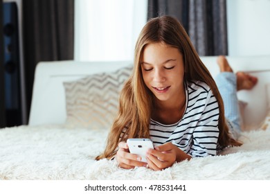 10 years old pre teen girl lying down on sofa and playing with smartphone