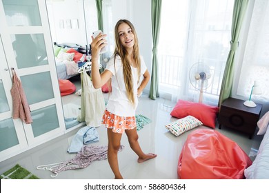 10 years old pre teen girl choosing outfit in her closet. Messy in the bedroom, clothing on the floor. Teenager is dressing up and taking selfie in the morning.