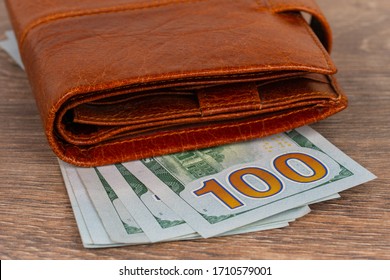 100 Dollars Banknotes With Orange Wallet On Wooden Table. Pension Or Unemployment Benefit Concept.