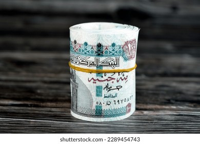 100 EGP LE one hundred Egyptian pounds cash money bills rolled up with rubber band, Egypt money roll pounds  features Sultan Hassan mosque and the Sphinx of Giza isolated on wooden background - Shutterstock ID 2289454743
