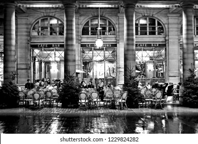 10.02.2016. People Sitting On The Outside Tables Of A Bar Cafe On A Rainy Night In Paris France