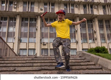 10.05.2019, Tula, Russia. A Little Boy Wearing Yellow Shirt And Baseball Hat Running Up And Down By Stairs. Kid Having Fun.