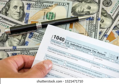 1040 tax form in hand and pen on dollars. Close-up.