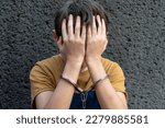 A 10-year-old boy in handcuffs sits on a gray background. Juvenile delinquent, criminal liability of minors. Members of youth criminal groups and gangs.