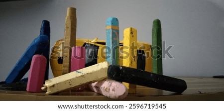 11 Crayons are posing in front of a miniature yellow Chevrolet Camaro that has rolled over.