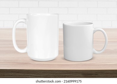 11 oz and 15 oz white coffee cups resting atop a light wood tabletop with modern white brick in the background.