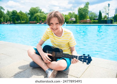 An 11 year old boy plays a black ukulele in front of the pool. - Powered by Shutterstock