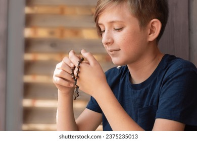 An 11 year old Catholic boy reads the rosary prayer, holds a wooden rosary with 10 beads in his hands. portrait of a boy with a wooden Catholic rosary during prayer.