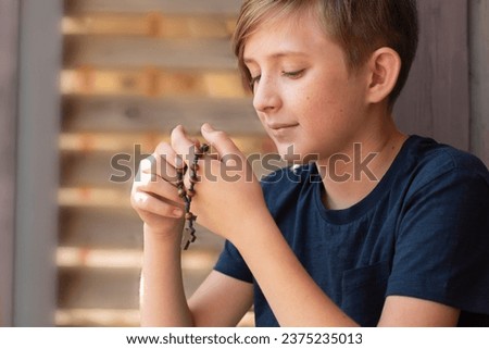 An 11 year old Catholic boy reads the rosary prayer, holds a wooden rosary with 10 beads in his hands. portrait of a boy with a wooden Catholic rosary during prayer. 商業照片 © 