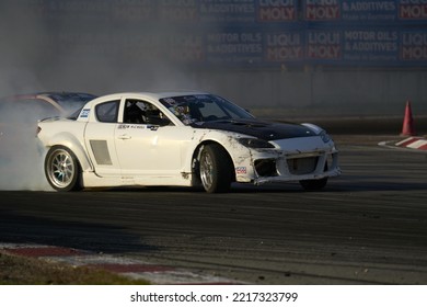 11-05-2022 Riga, Latvia A Car With A Lot Of Smoke Coming Out Of It, A White Sports Car Speeding On A Track At Night.