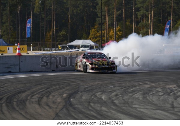 11-05-2022 Riga, Latvia a car with a lot of smoke\
coming out of it, a person driving a car on a race track with a\
burn out tire.