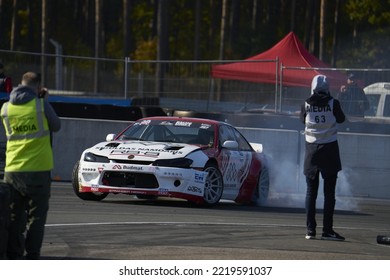 11-05-2022 Riga, Latvia A Man Standing Next To A Car On A Race Track, A Car That Is Doing A Burn Out On A Track.