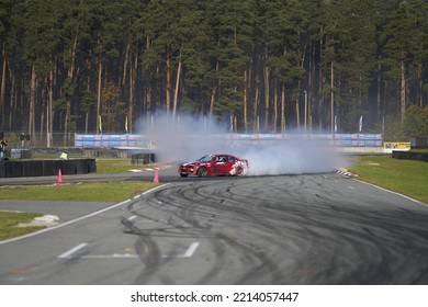 11-05-2022 Riga, Latvia A Red Car Driving On A Track With Smoke Coming Out Of It, An Action Stunt Vehicle Drifts Along A Track.