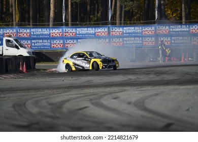 11-05-2022 Riga, Latvia A Yellow And Black Car On A Track With Smoke Coming Out Of It, A Small Car Doing An Burn Out During A Race.