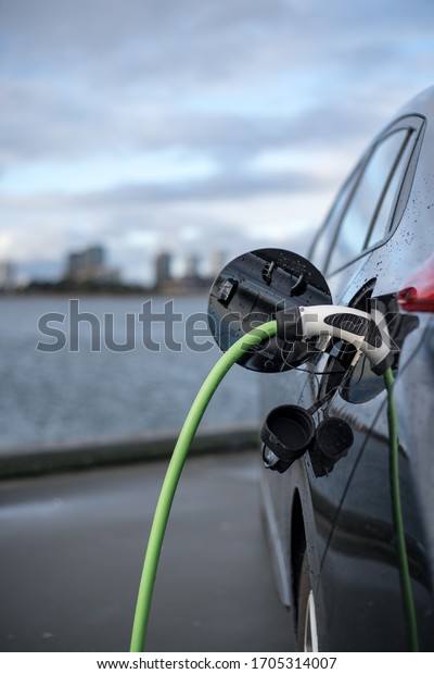 11-20-2020, Copenhagen, Denmark - Charging an\
electric car, with the city and water in the background, green\
charging cable and black car.\
copenhagen