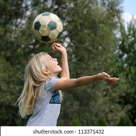 11-year old blond girl playing with a football, reaching to head the ball - Powered by Shutterstock