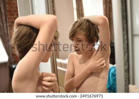 An 11-year-old boy stands in front of a mirror, raised his hand and looks at the hair in his armpit. a teenager explores the changes in his body during puberty.