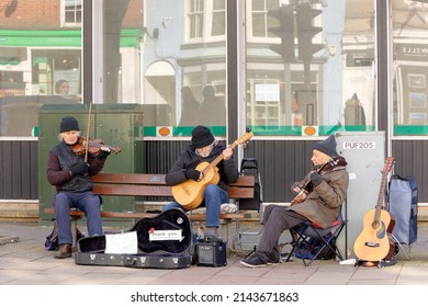 12 FEBRUARY 2022 Three Elderly Gentlemen Sitting Busking On The High Street In Lymington, Hampshire Playing Guitars And Violins, Guitar Case Used For Money Collection, Space For Text