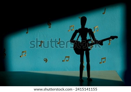 A 12 inch wooden drawing mannequin figure silhouette plays a bass guitar against a blue backdrop with gold musical notes and treble and bass clefs