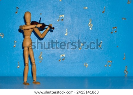 A 12 inch wooden drawing mannequin figure plays a violin against a blue backdrop with gold musical notes and treble and bass clefs