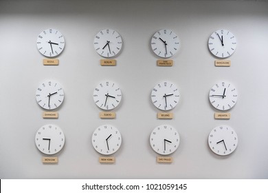12 wall clocks on the white wall of business office space showing time of different capital cities of the world.