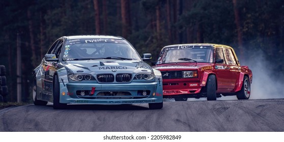 12-05-2022 Riga, Latvia. Two Cars On A Track Racing In Front Of One Another, Two Cars Side By Side Next To Each Other.