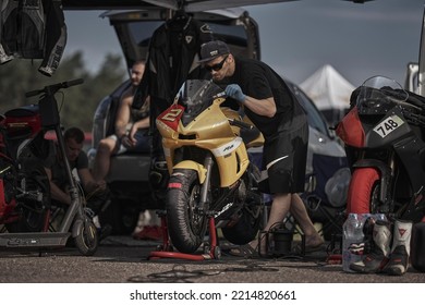 12-09-2022 Riga, Latvia A Man Working On A Yellow Motorcycle In A Parking Lot, A Man Is Fixing A Motorcycle With A Black Hat.