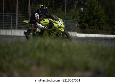 12-09-2022 Riga, Latvia A Person Riding A Yellow Motorcycle On A Track, Person Riding Motorcycle On Asphalt Road In Open Field.