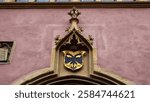 12.12.2024, Colmar, France. A Gothic-style emblem of the Holy Roman Empire on a historic building facade. The intricate stone carvings and golden crest highlight Colmar’s medieval heritage.