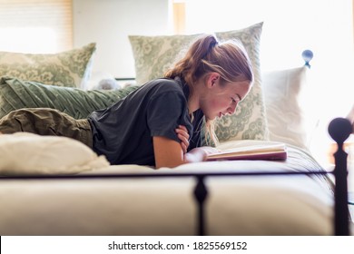 13 Year Old Girl Lying In Her Bed Reading By Window Light