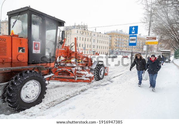 13.02.2021, Russia,\
Moscow. Clearing the road from the snow cover after the snowfall by\
tractor with a\
bucket
