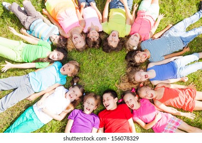 14 Kids Laying In A Circle In The Grass With Happy Faces Shoot From Above