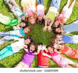 14 Kids Laying In A Circle In The Grass With Happy Faces Shoot From Above Lifting Hands Above 