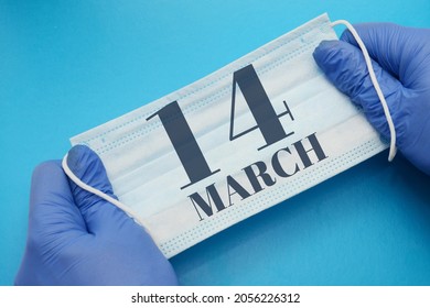 14 March Day Of Month. Doctor Holding An Antivirus Mask In Blue Medical Gloves On A Blue Background. Protection From Disease