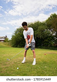 14/06/2020, London, England Young male man boy playing golf on his own about to drive the golf ball with his club mid swing. Burning off steam and getting his daily exercise in shorts on a sunny day  - Shutterstock ID 1785915449