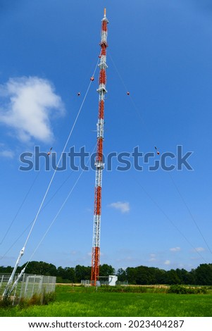 149m high mast, a transmitter for VHF radio and television in Hemmingen, a town in the Hannover region. Red and white radio communication station against bright blue sky.