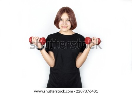 A 14-year-old teen girl works out at home with dumbbells, the girl is happy and healthy after constant training in the morning or in the evening, the girl is very fond of fitness and athletics