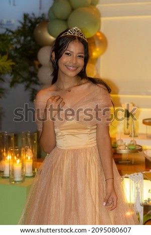 A 15-year-old brunette Caucasian girl celebrates her birthday wearing a tiara and an elegant dress.
