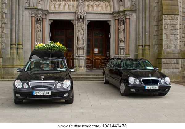 16 March 2018 A hearse and a funeral car parked\
outside St Colman\'s Cathedral in Cobh Cork Ireland during a service\
for a local dignatary