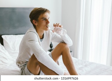 16 Years Old Teenage Boy Drinking Mineral Water While Sitting In Bed In His Room After Waking Up In The Morning