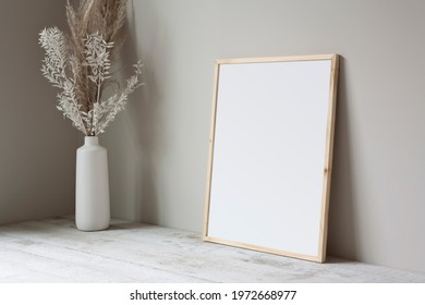16x20 thin wooden, vertical frame mockup, lying on a white wooden floor with a pampas grass prop. - Shutterstock ID 1972668977